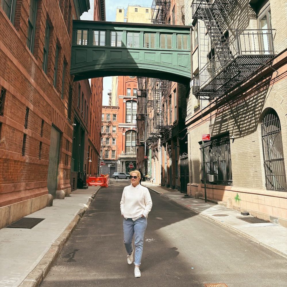 Woman walking down a New York City Alley with brick buildings and green bridge